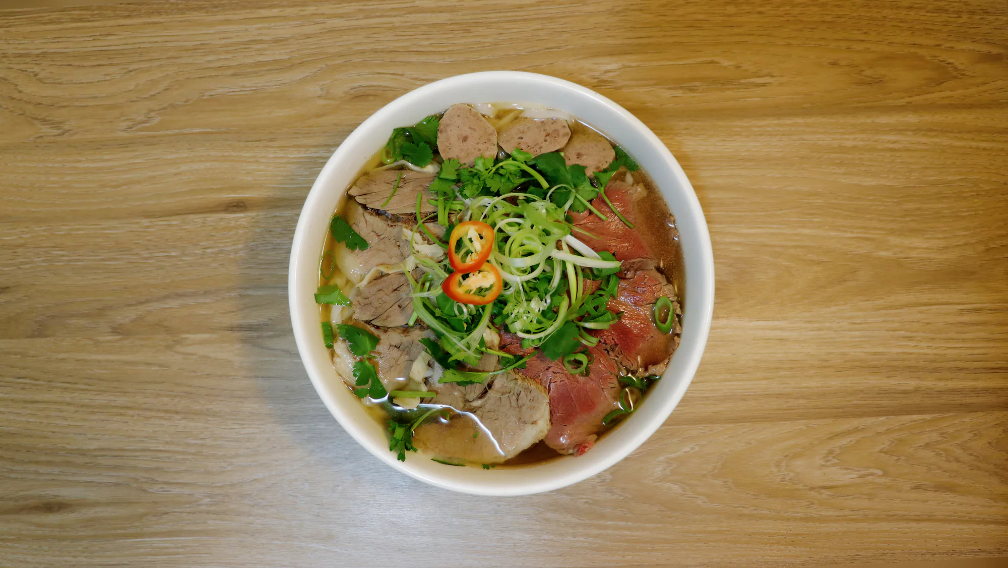 Beef phở photographed from above on a wooden table.