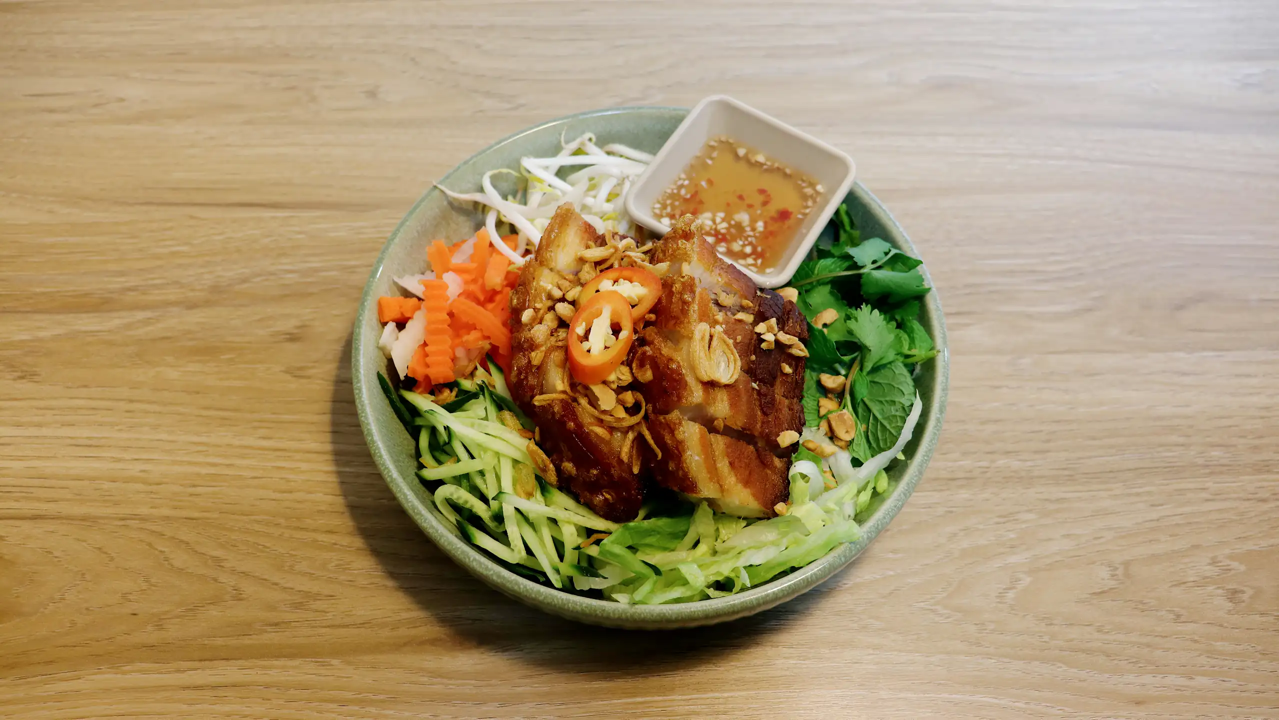 A crispy pork belly vermicelli bowl with salad, herbs and dipping sauce.