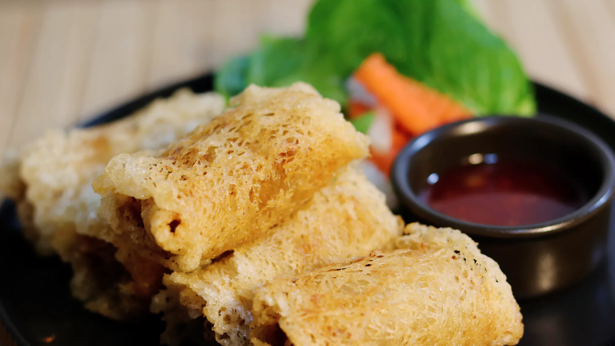 Five golden spring rolls served with lettuce, pickled carrot and dipping sauce.