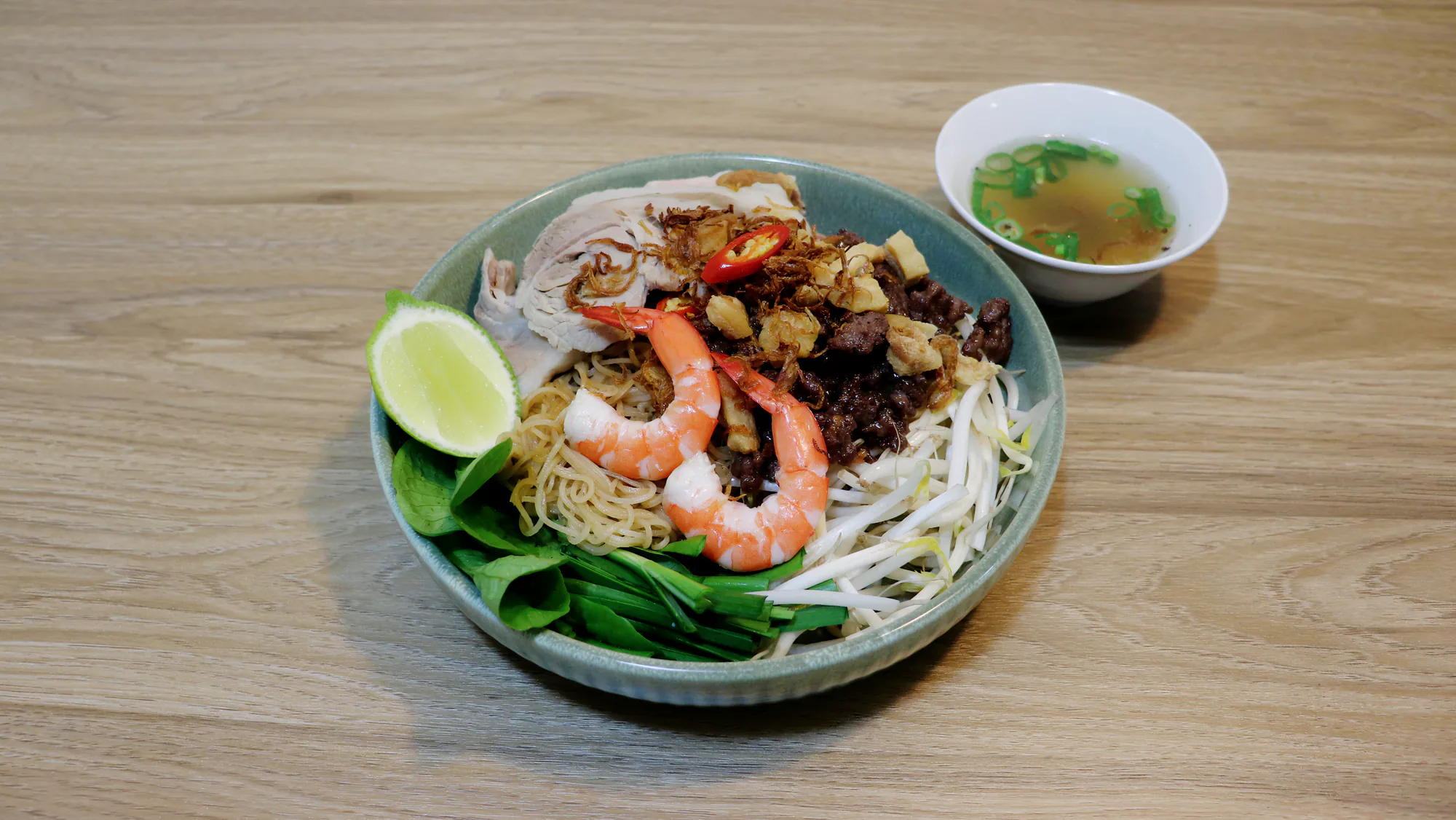 Vietnamese pork and seafood noodle soup with herbs and sliced chilli.